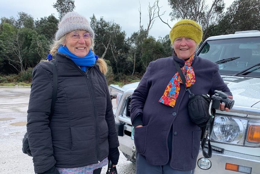 Two older women stand next to a car