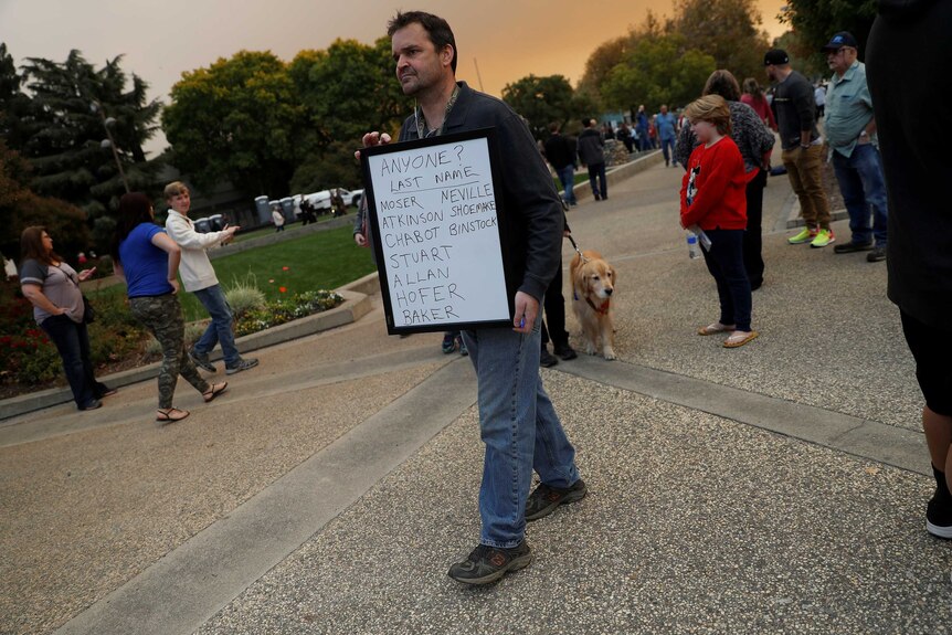 A man walks around holding a sign with surnames written on it.