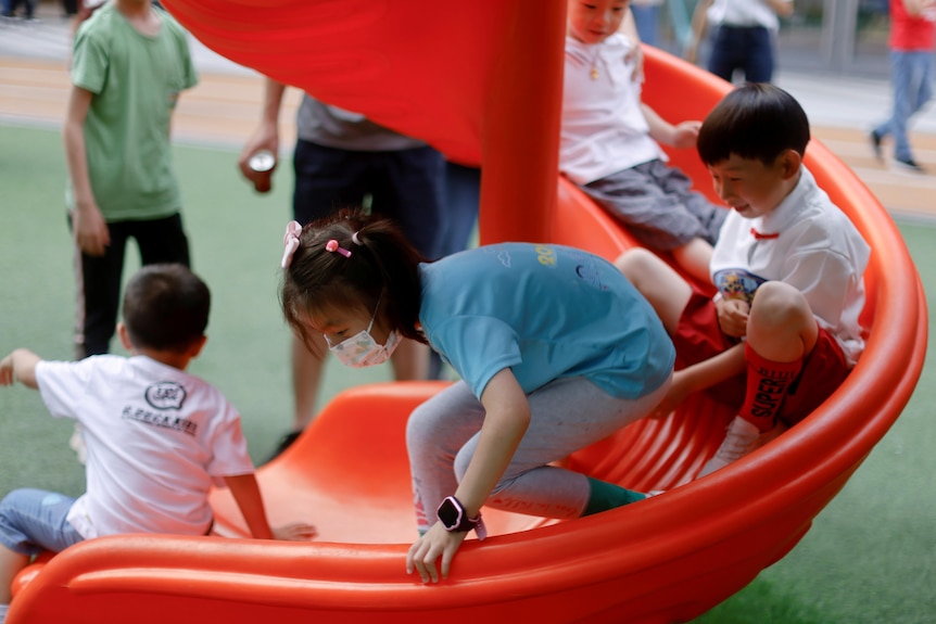 Four young children use a spiralling red slide in a playground inside a shopping centre.