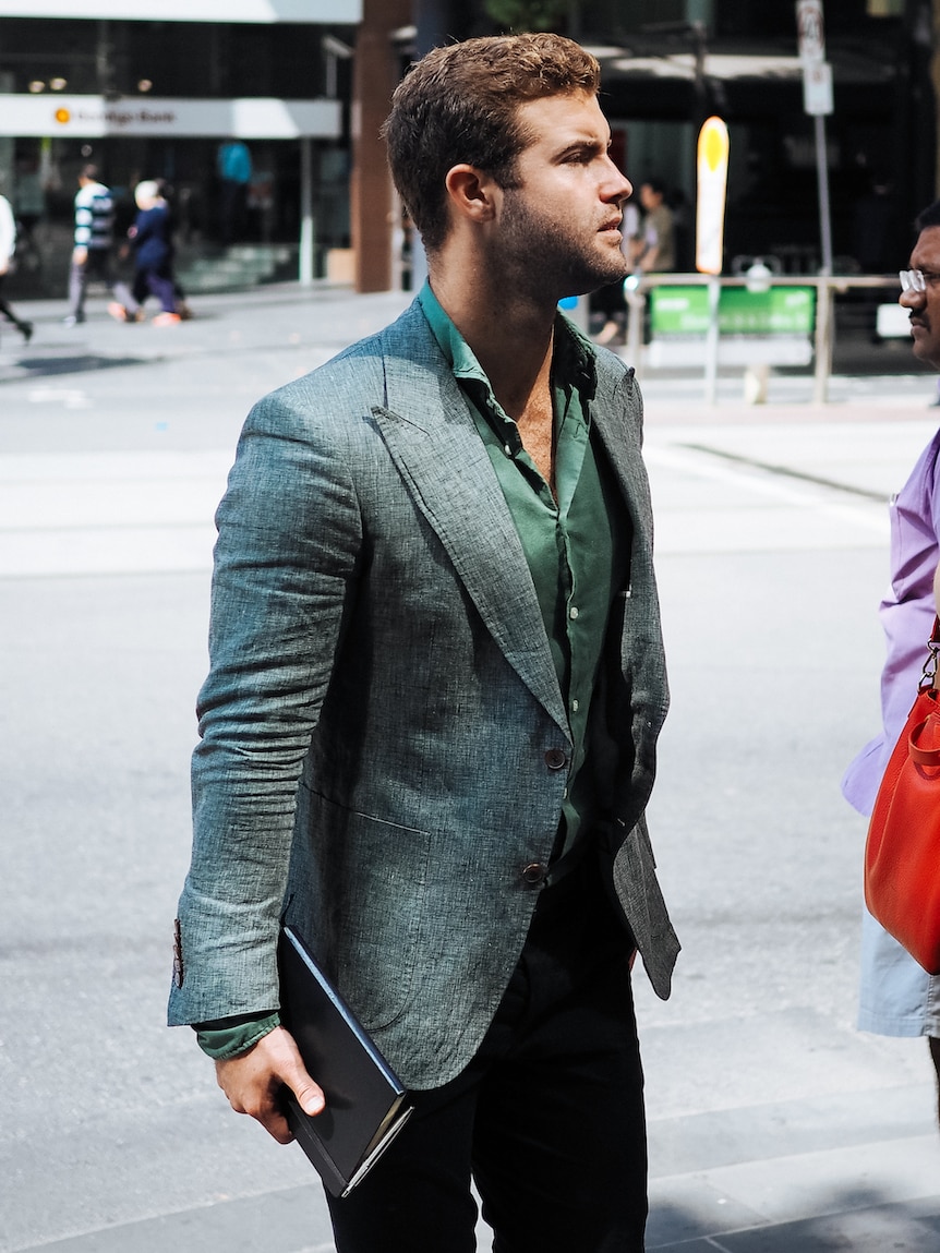 A man in a silk shirt and blazer, in emerald hues, walks through a Melbourne street.