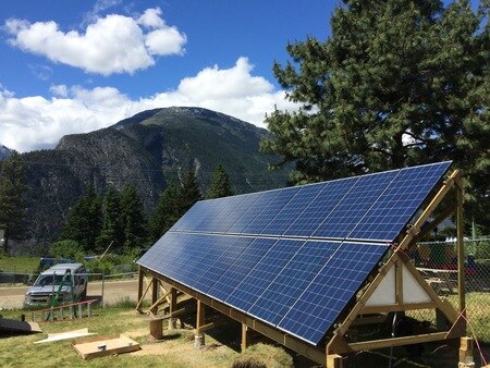 A solar panel sits in a green field in front of a mountain