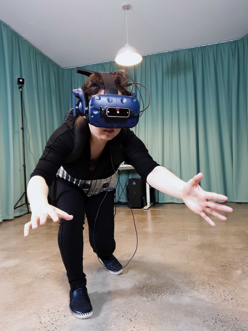 Artist Eugenie Lee with a VR headset and haptic belt on in a room with curtains in the artwork Breakout My Pelvic Sorcery