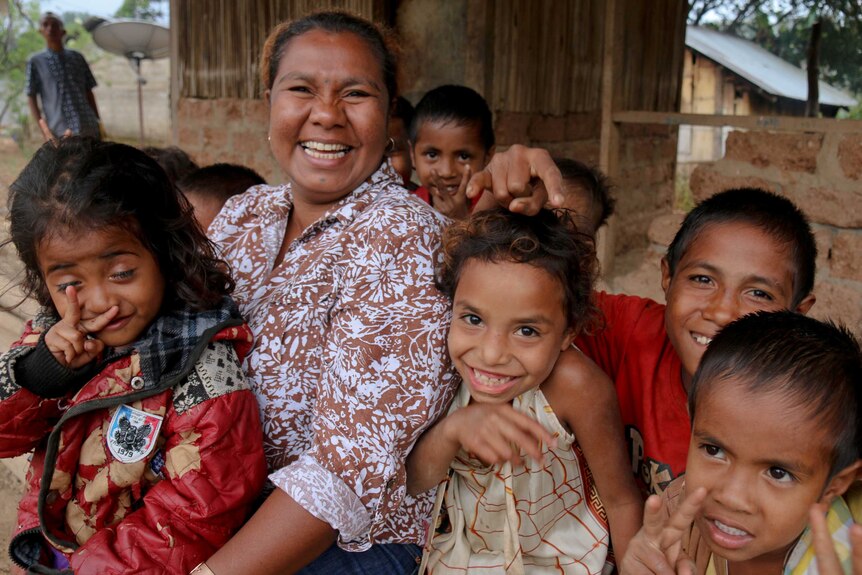 Timorese woman smiling with children on her lap and around her.