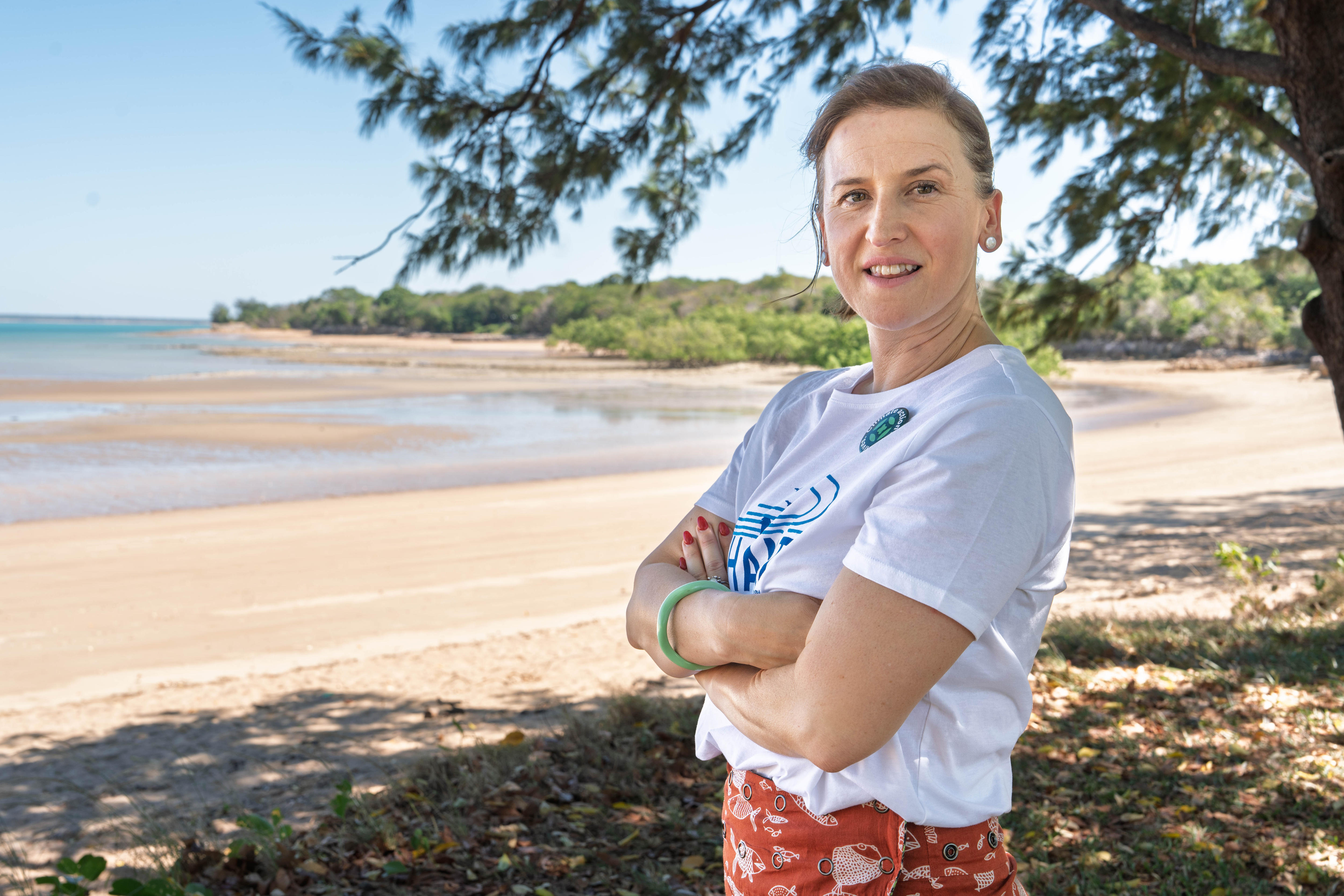 A woman folds her arms while standing on a tropical beach.