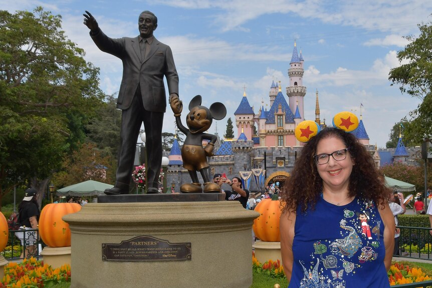 Jodi Eichler-Levine wearing Mickey Mouse ears in front of a statue of Walt Disney and Mickey Mouse at a Disney theme park.