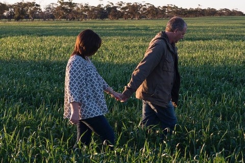 A woman and a man walking through a green field holdings hands
