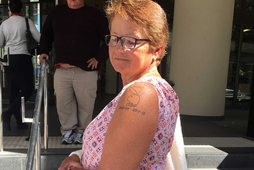 Marilyn Townsend stands sideways to the camera looking at a tattoo on her shoulder outside court.
