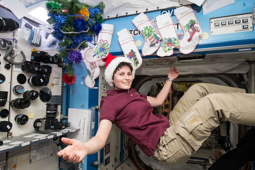 A woman wearing a purple top and a santa hat floating in mid air in a space ship