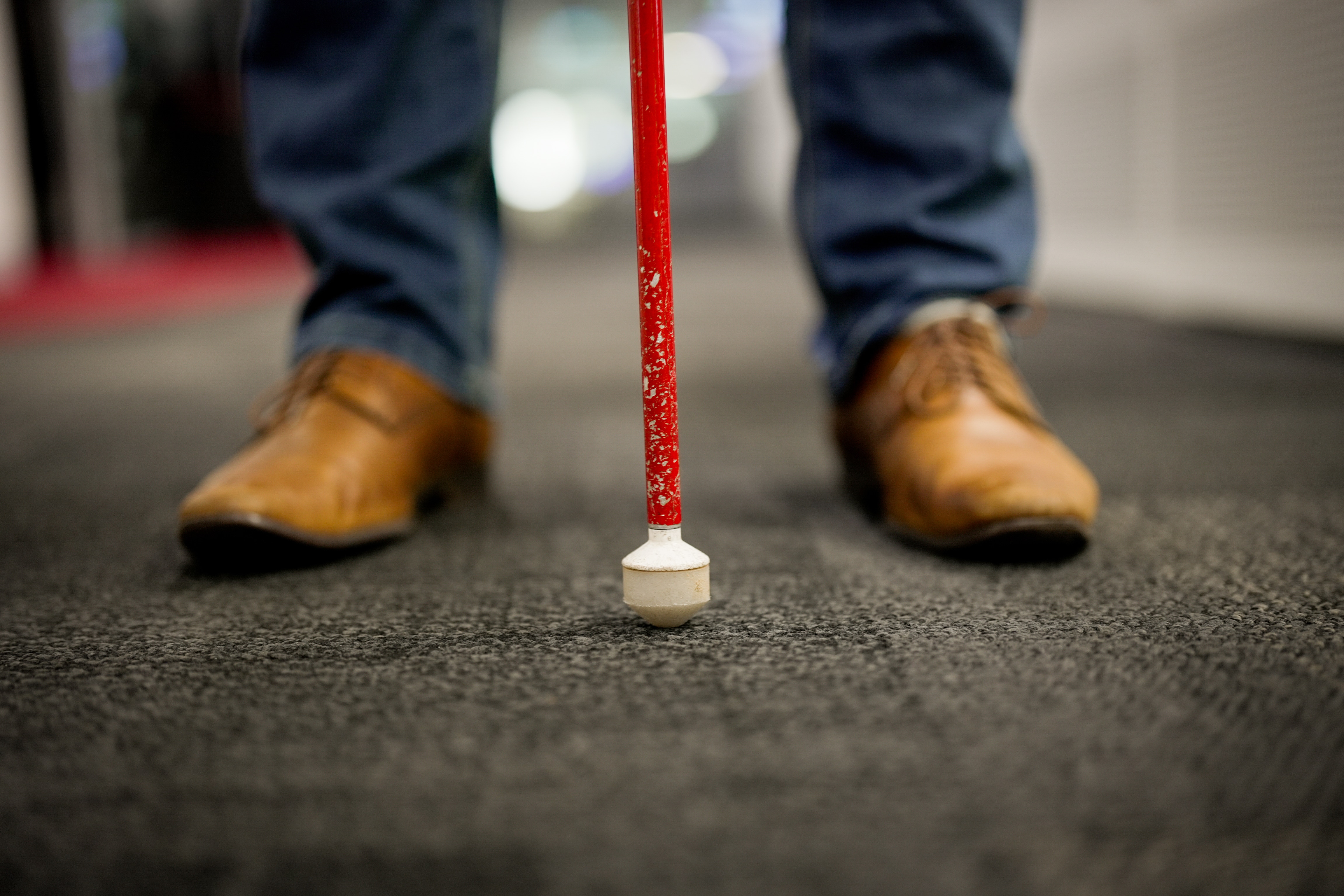 A man's feet are shown in leather shoes with a cane used by blind people resting on the floor