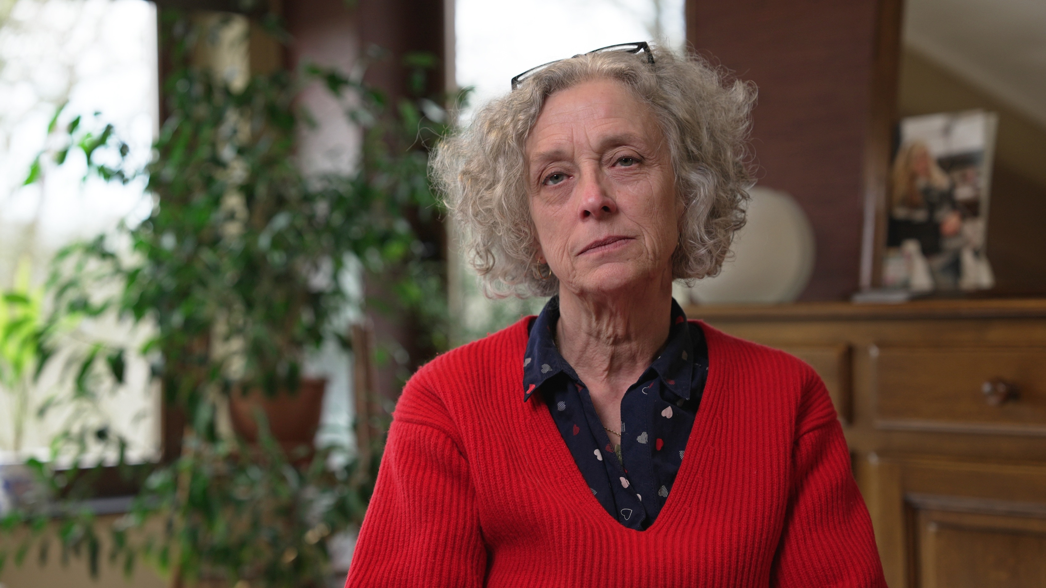 Ariane Mathieu, la madre de Céline Cremer, sentada en un salón, vestida con un jersey rojo y una expresión seria en el rostro.