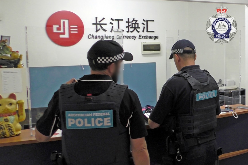 Two federal police officers are shown from behind at a Changjiang Currency Exchange outlet.