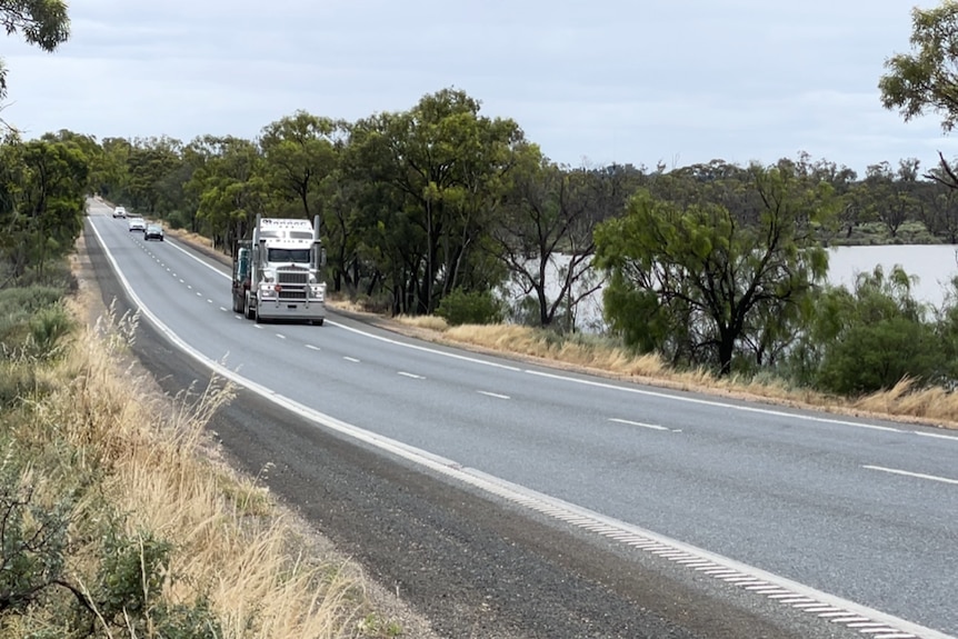 A truck travels along a wide road with water on either side.
