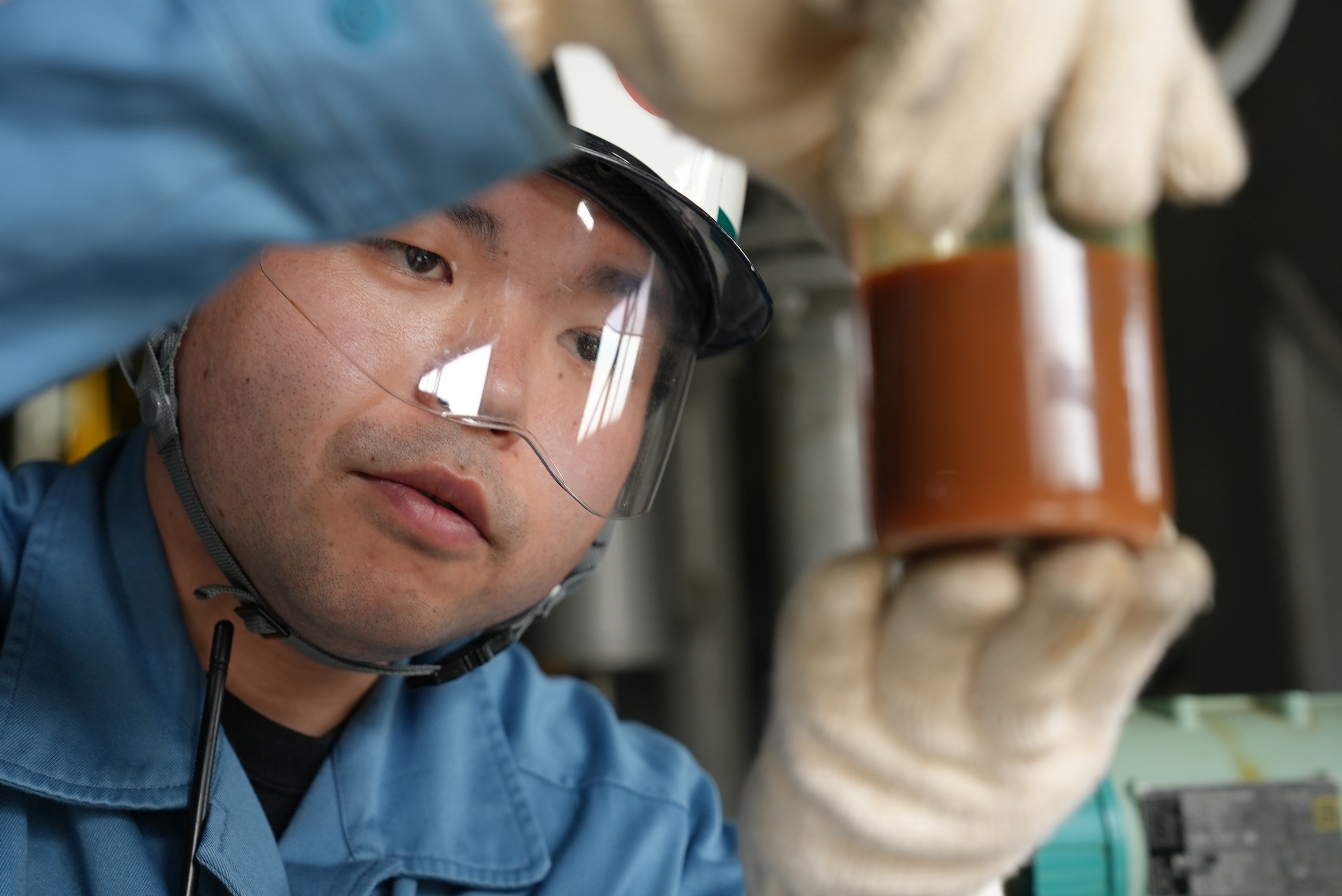 A close up of a Japanese man wearing a face shield measuring eqipment.