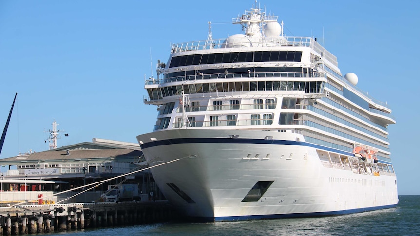 A large white cruise ship docked at a jetty.