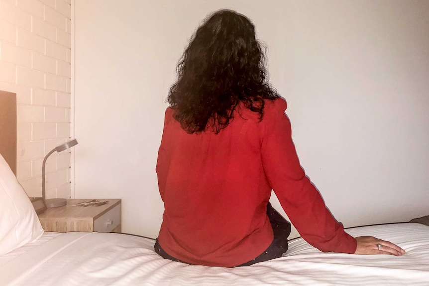 An unidentified woman sits on a hotel bed.