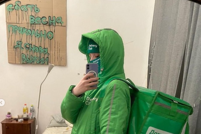 A woman in a bright green delivery driver uniform takes a mirror selfie
