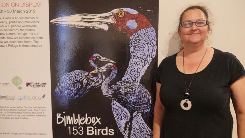 Woman stands next to Bimblebox 153 Birds sign