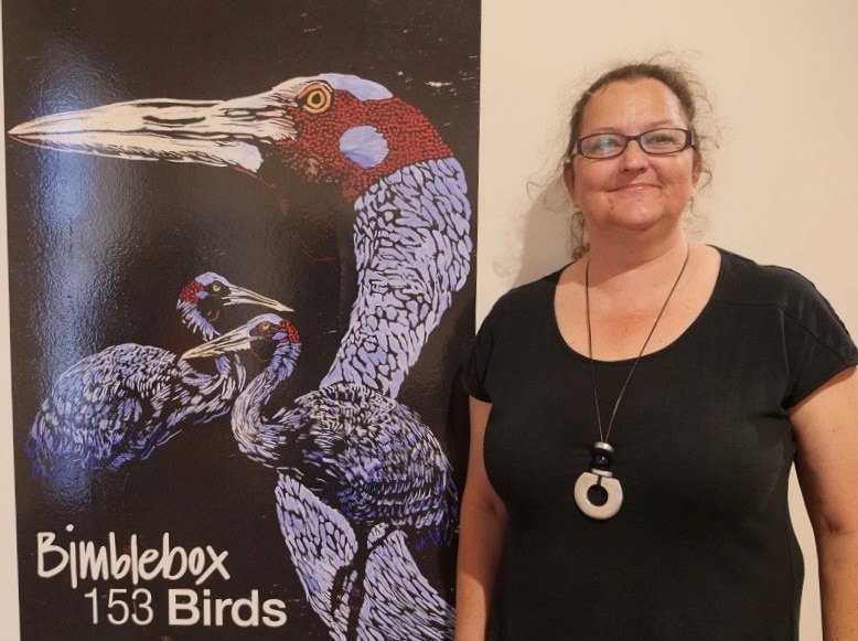 Woman stands next to Bimblebox 153 Birds sign