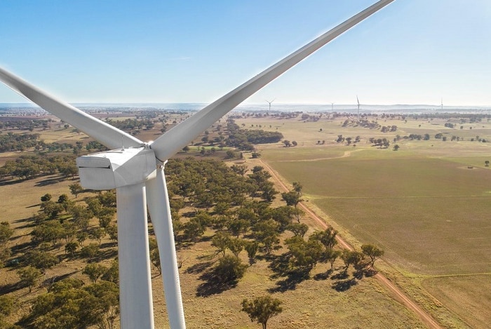 An image from the air shot from behind a wind turbine, looking over paddocks and a number of other turbines.