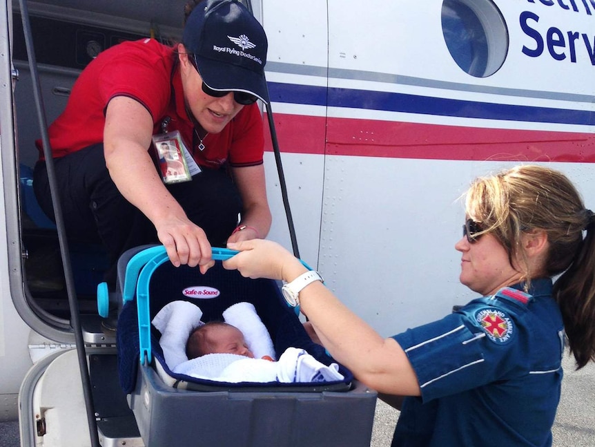 An ambulance officer passes a baby in a capsule up to RFDS midwife in plane