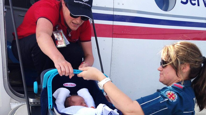An ambulance officer passes a baby in a capsule up to RFDS midwife in plane