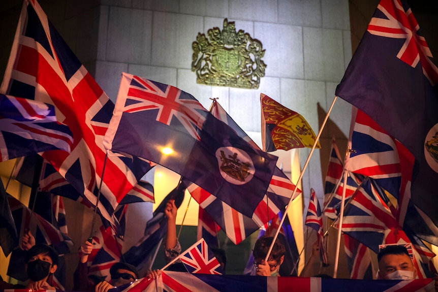 A crowd of protesters wave Britain's union jack flag and Hong Kong's British colonial flag in front of the British coat of arms.