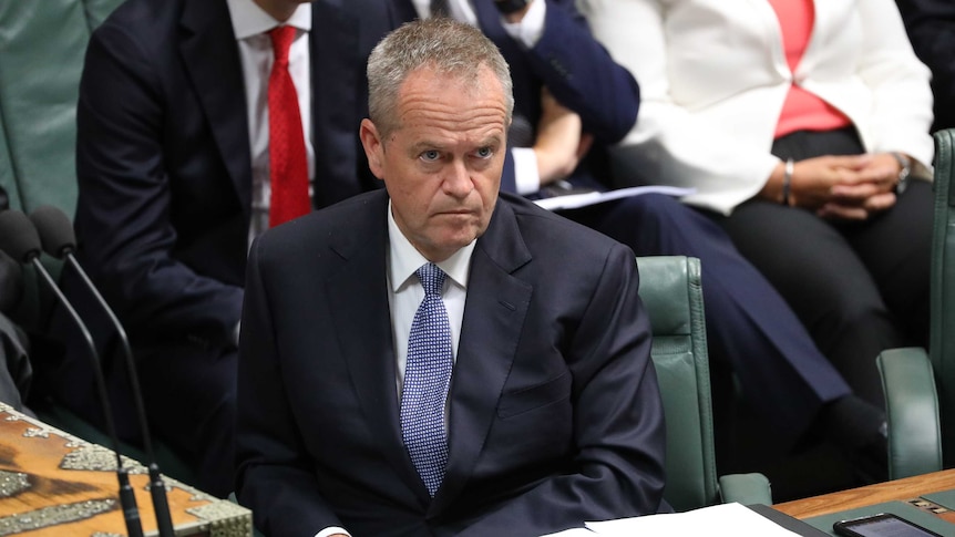 He's sitting in his seat, furrowed brow, blue tie, hands in lap.