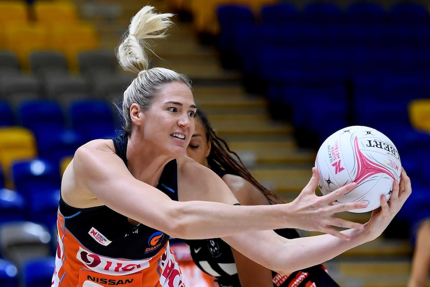 A Giants Super Netball player turns to the left to catch the ball with both hands against Collingwood.