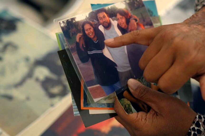 A person's hands hold a photo of two women and a man with their arms around each other.
