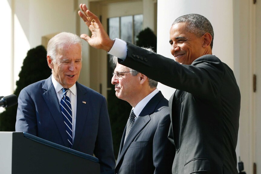 Barack Obama waving while Joe Biden speaks to Merrick Garland