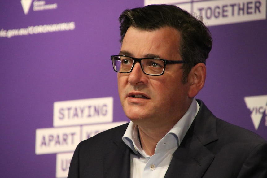 Daniel Andrews wearing a suit and glasses, addressing the media.