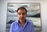 David Van Rooy sitting at an office desk with a grey and white picture behind his head.