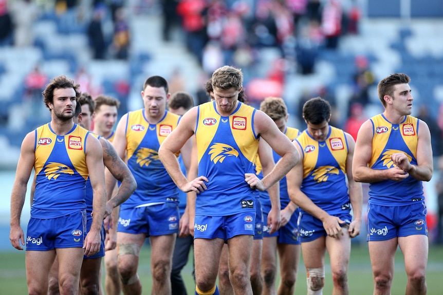 A group of dejected West Coast Eagles players trudge off the field with heads bowed after losing a game.