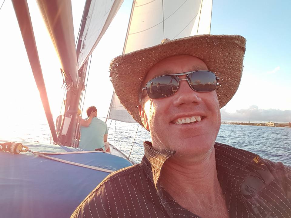 a man smiles at the camera on a boat, wearing sunnie and smiling at the camera