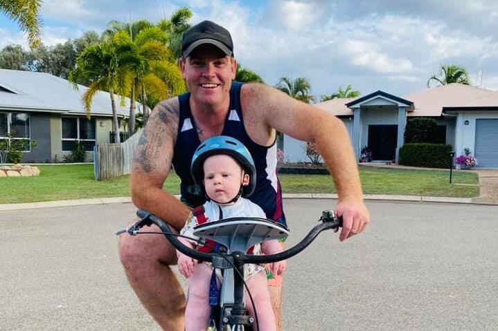 A man on a bike with a baby on the street