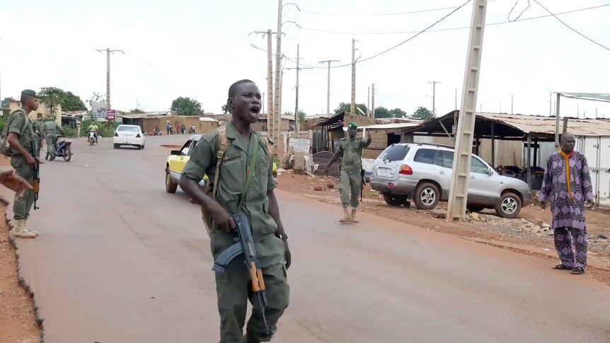 Men in green uniforms and military rifles on a road in an African township.