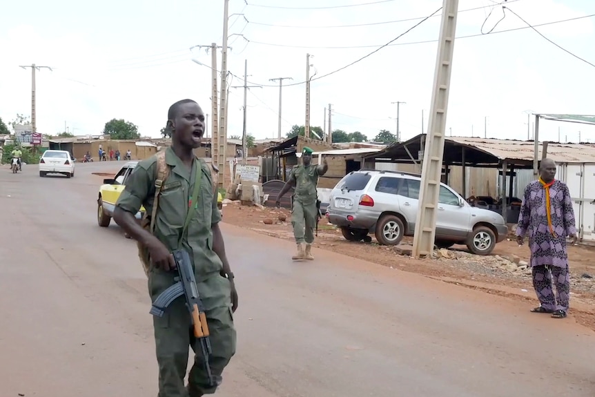 Men in green uniforms and military rifles on a road in an African township.