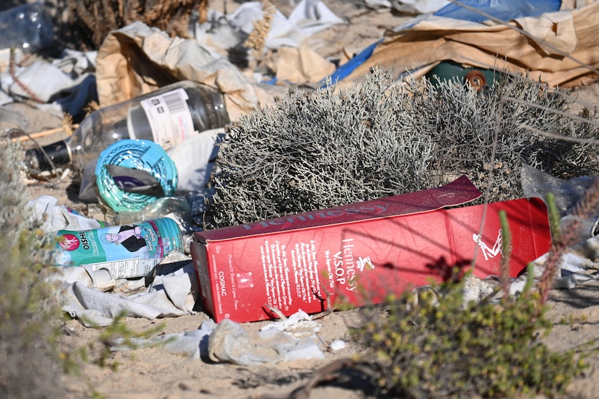 A pile of discarded bottles and other rubbish in sand dunes