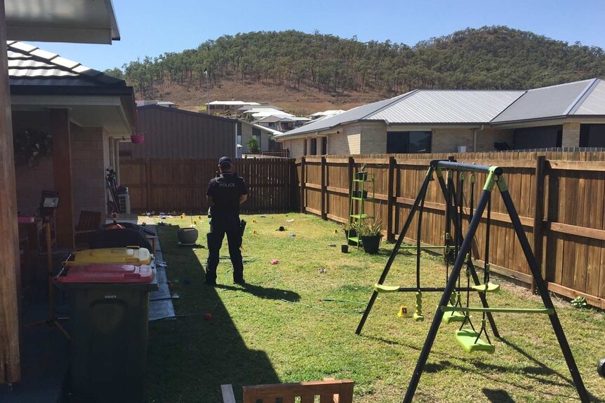 A police officer stands in the backyard of a Rockhampton house, , surrounded by forensic markers.