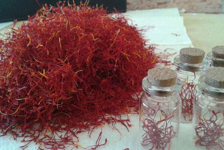 A bunch of red and yellow saffron threads sit on a table next to small glass containers.