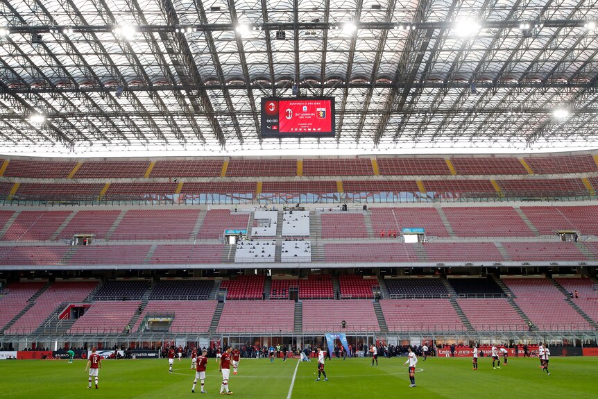 Players from AC Milan and Genoa line up in an empty stadium