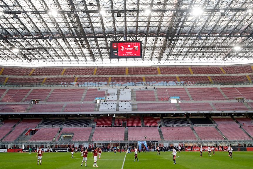 Players from AC Milan and Genoa line up in an empty stadium