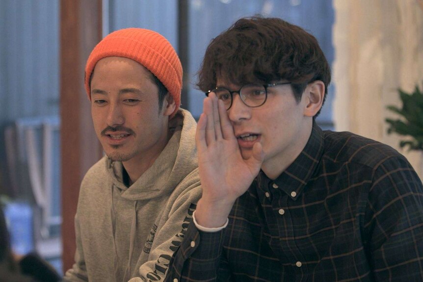 Two young Japanese men, one with his hand up to his face as if he's telling a secret, on the TV show Terrace House
