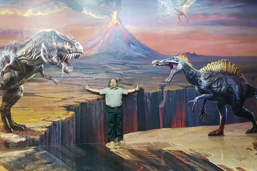 Sutopo Nugroho posing in front of an image of dinosaurs