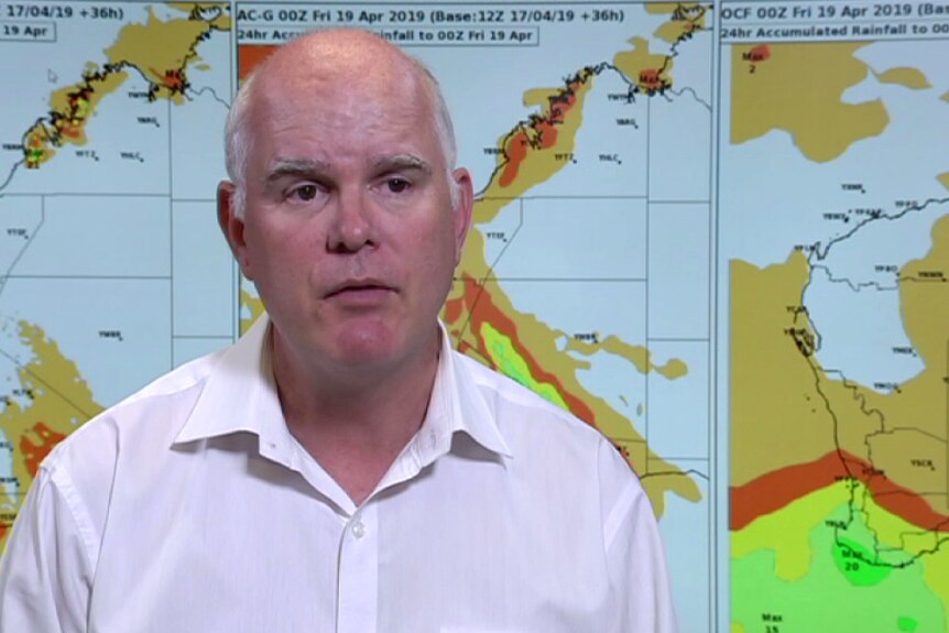 A man talking in front of screens displaying weather maps