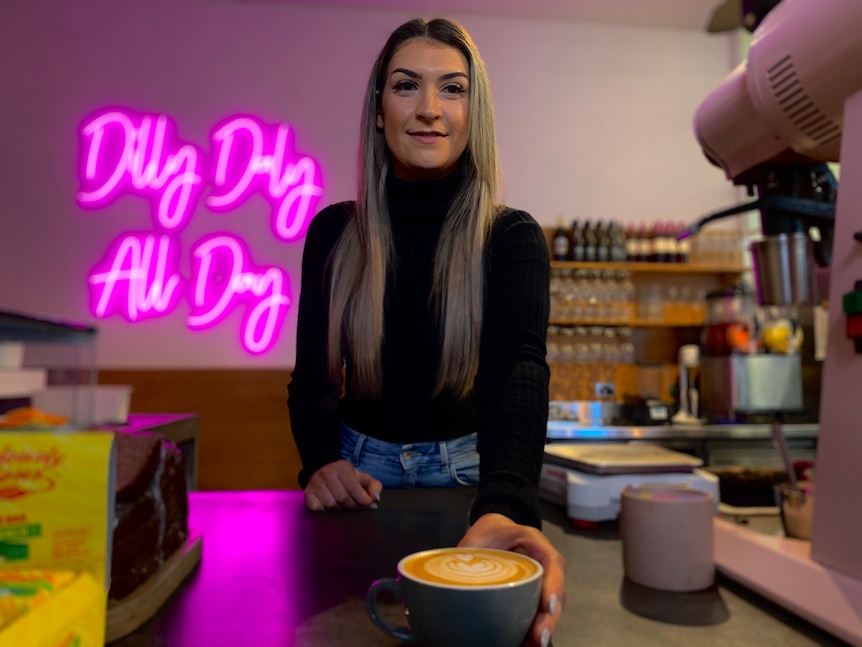 A woman in a black turtleneck stands in front of a neon sign.