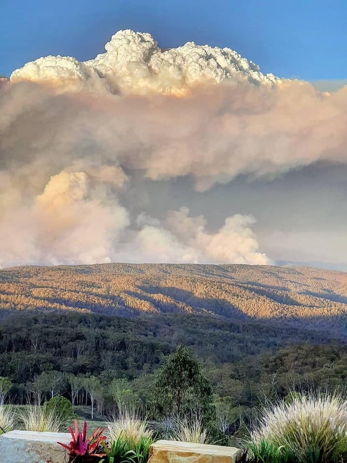 A huge smoke cloud over a large landscape of hills and trees.