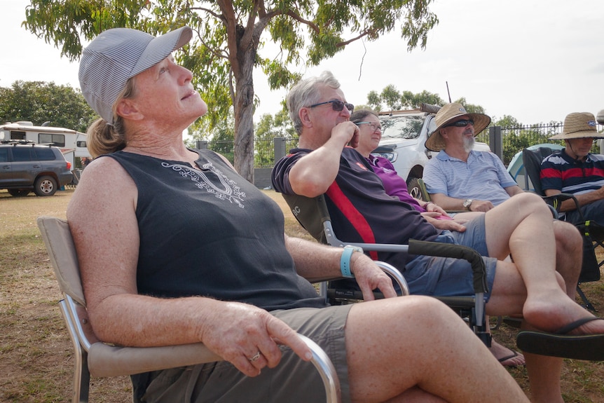 Two women and three men sit in camping chairs in a campground gazing into the sky.