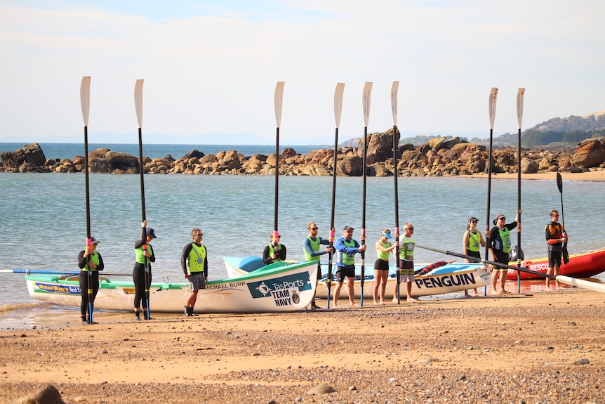 Rowers raise their oars as they stand on the waterfront