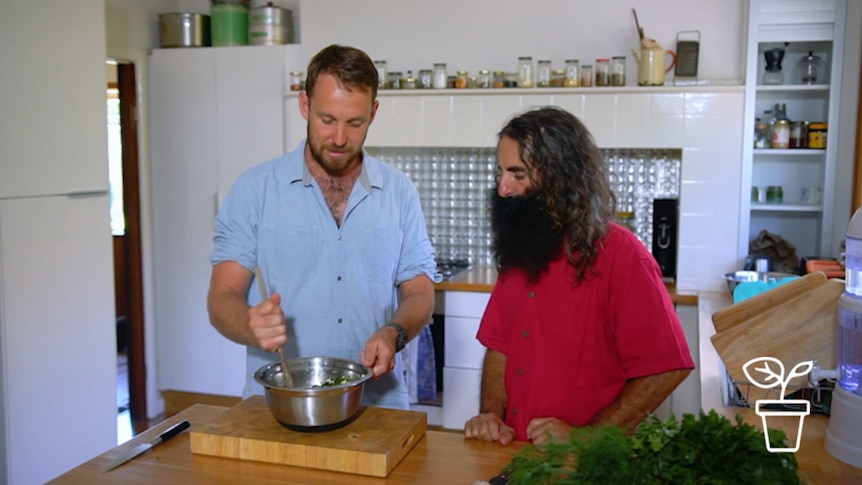 Presenter watches on as man stirs food in metal bowl in kitchen